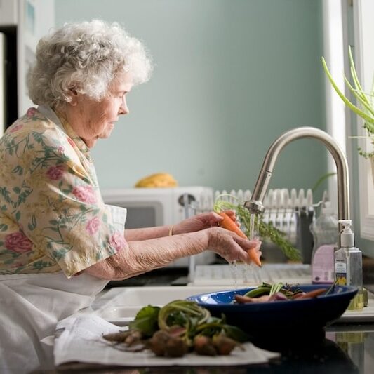 elderly woman living at home, washing vegetables in her kitchen